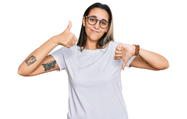 Young hispanic woman wearing casual white t shirt doing thumbs up and down, disagreement and agreement expression. crazy conflict