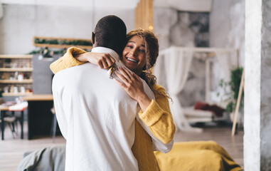 Radiant woman in a yellow sweater embraces man from behind, her face alight with happiness, holding...