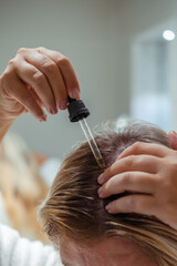 Woman applies oil to her hair with pipette. Beauty caring for scalp and hair