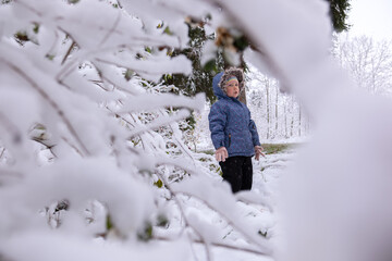 Little beautiful girl in winter clothes standing alone in the middle of a snowy forest. Girl in jacket with fur hood posing in winter forest. Shrubs and trees are covered with snow