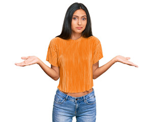 Young brunette arab woman wearing casual clothes clueless and confused expression with arms and hands raised. doubt concept.