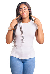 Obraz na płótnie Canvas Young african american woman with braids wearing casual clothes smiling cheerful showing and pointing with fingers teeth and mouth. dental health concept.