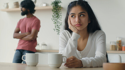 Upset Indian woman wife thinking of relationship problems after quarrel with husband on kitchen offended man stand background. Married diverse multiracial couple arguing having conflict disagreement - obrazy, fototapety, plakaty