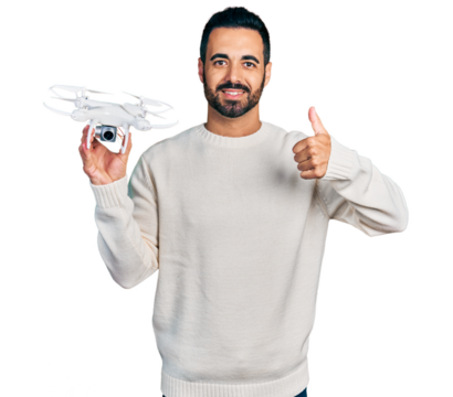 Young hispanic man with beard holding drone smiling happy and positive, thumb up doing excellent and approval sign