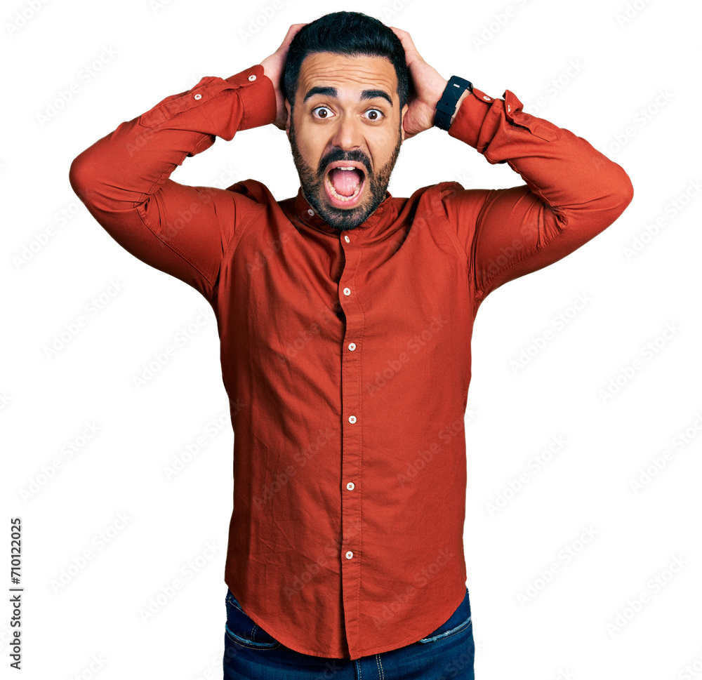 Wall mural Young hispanic man with beard wearing casual shirt crazy and scared with hands on head, afraid and surprised of shock with open mouth