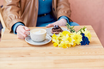 Cozy coffee break - woman enjoying latte and chocolate dessert with spring daffodils