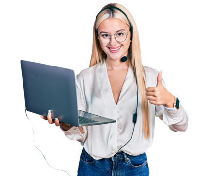 Beautiful blonde woman working with laptop wearing operator headset smiling happy and positive, thumb up doing excellent and approval sign