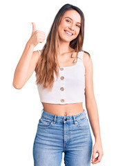 Young beautiful girl wearing casual sleeveless t shirt doing happy thumbs up gesture with hand. approving expression looking at the camera showing success.