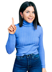 Young brunette woman with blue eyes wearing casual turtleneck sweater smiling with an idea or question pointing finger up with happy face, number one