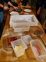 A view of fresh ingredients in containers and hands preparing homemade pizza on a wooden table - 710128884