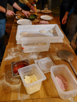 A view of fresh ingredients in containers and hands preparing homemade pizza on a wooden table