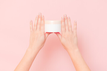 Round jar of cosmetic cream in hand on pink background. Cosmetics beauty mockup for product branding