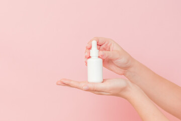 Hand holding glass cosmetic bottle for serum (hyaluronic acid and collagen) on pink background. Beauty concept