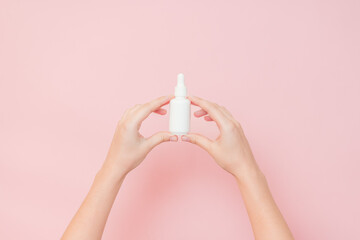 White bottle with serum lotion or essential oil (hyaluronic acid and collagen) in hands on pink...