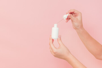 Hand holding glass cosmetic bottle for serum (hyaluronic acid and collagen) on pink background. Beauty concept