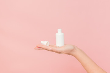Hand holding glass bottle with dropper lid. White container with cosmetic product, serum (essential oil ) on pink background. Concept of beauty