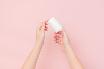 View on white bottle plastic tube in hands on pink background. Packaging for pills, capsules,...