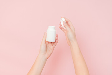 White bottle plastic tube in woman's hands on pink background. Packaging for pills, capsules or supplements. Cosmetics