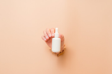 White bottle with serum lotion or essential oil (hyaluronic acid and collagen) in hand on beige background. Skin care cosmetics concept, beauty flyer