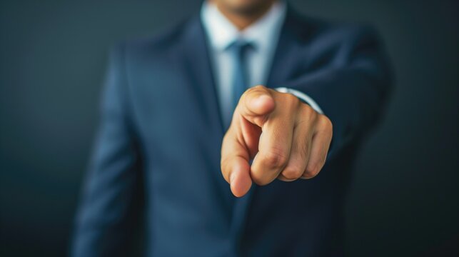 Close-up of a businessman in a navy blue suit pointing directly at the camera with a focused expression, choice concept