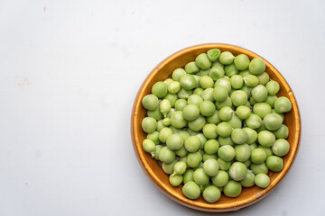 Top view of a brown saucer of green peas, fresh peas on a white background