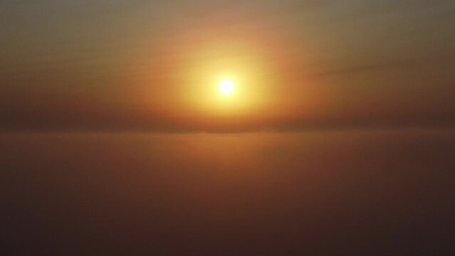 Toma a&eacute;rea atravesando un mar de nubes en un amanecer con el sol en el centro del horizonte