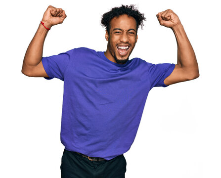 Young african american man with beard wearing casual purple t shirt celebrating surprised and amazed for success with arms raised and open eyes. winner concept.