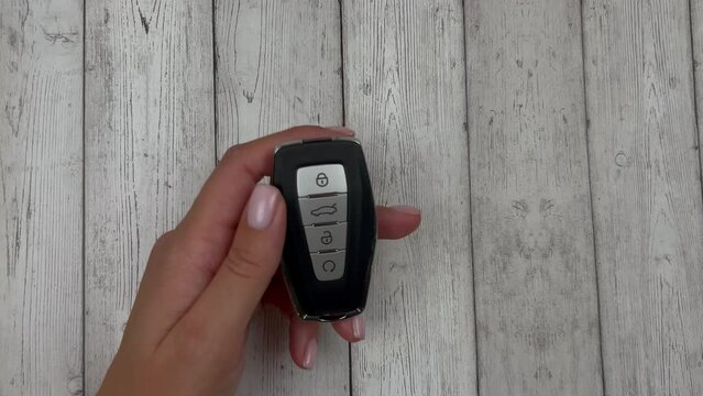 The car keys are black with metal inserts and automatic buttons, a white European hand picks up on a white wood background by pressing the trunk opening button. High quality 4k footage