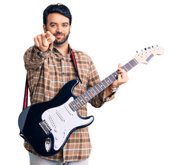 Young hispanic man playing electric guitar pointing with finger to the camera and to you, confident gesture looking serious