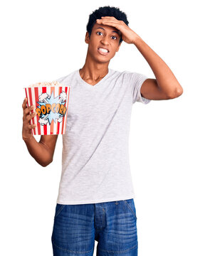 Young african american man holding popcorn stressed and frustrated with hand on head, surprised and angry face