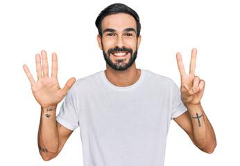 Young hispanic man wearing casual white t shirt showing and pointing up with fingers number seven...