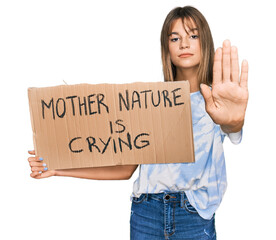 Teenager caucasian girl holding mother nature is crying protest cardboard banner with open hand doing stop sign with serious and confident expression, defense gesture