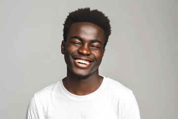 A handsome young African-American man in a white T-shirt is blinking his eyes with pleasure, wearing a happy expression. The concept of human facial expressions and emotions - obrazy, fototapety, plakaty