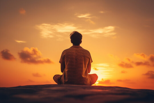 Man is seen sitting on top of beach as sun sets. This image can be used to depict relaxation, solitude, or enjoying beauty of nature.
