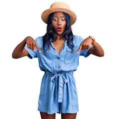 Young indian girl wearing summer hat pointing down with fingers showing advertisement, surprised face and open mouth