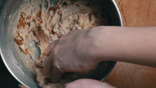 Female hands knead dough with candied fruits for stollen in slow mo. Raw dough for home baking. Traditional homemade Christmas German stollen pie in the kitchen at home.