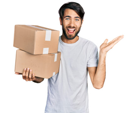 Hispanic man with blue eyes holding packages celebrating victory with happy smile and winner expression with raised hands
