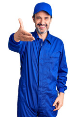 Middle age handsome man wearing mechanic uniform smiling friendly offering handshake as greeting and welcoming. successful business.