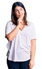 Young beautiful brunette woman wearing casual t-shirt with hand on chin thinking about question, pensive expression. smiling with thoughtful face. doubt concept.