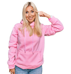Obraz na płótnie Canvas Young blonde woman wearing casual sweatshirt smiling pointing to head with one finger, great idea or thought, good memory