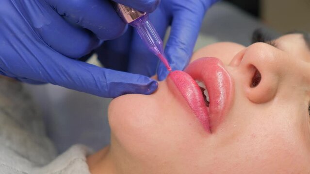 Young woman having permanent makeup on lips in beautician salon. Close up