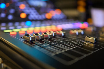 An expert adjusting audio mixing console with white blank screen laptop on control desk.
