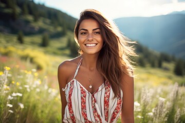 A radiant woman with a captivating smile, wearing a striped romper with a cinching waist belt, standing in a sunlit meadow filled with wildflowers, with a picturesque mountain range in the background - obrazy, fototapety, plakaty
