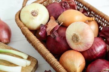 Board and wicker basket with different kinds of onion on white wooden background