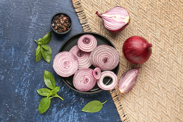 Plate with fresh onion slices and spices on blue background