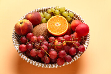 Wicker bowl with different fresh fruits on orange background