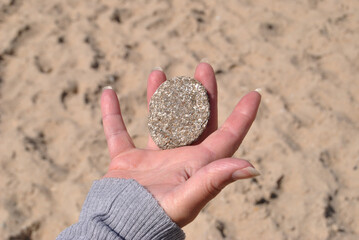 A woman's hand holding, protecting or contemplating a rounded stone with beach sand in the...