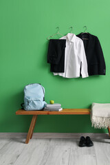 Bench with backpack, shoes and stylish school uniform hanging on green wall in room