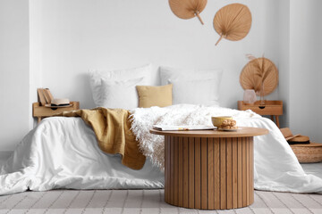 Cozy bed with white blanket and coffee table in interior of light bedroom