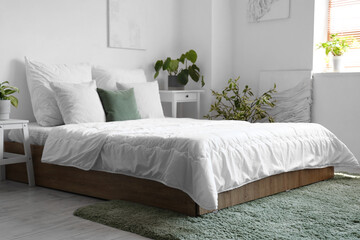 Cozy bed with white blanket and pillows in interior of light bedroom